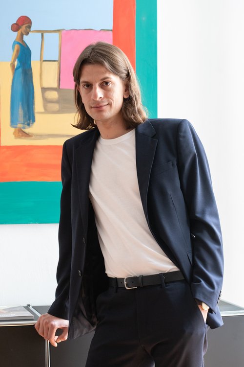 Ansgar Gumb steht vor einem Gemälde angelehnt an ein Regal